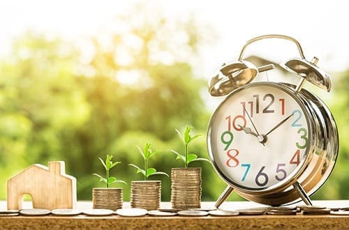Stacks of coins with saplings growing from them between house and clock your financial planner